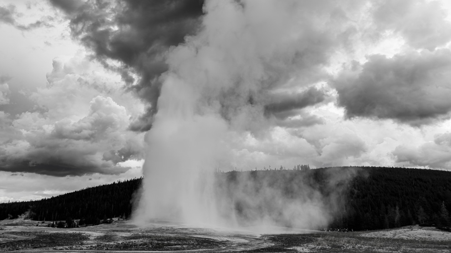 Old Faithful erupting beneath storm clouds in Yellowstone National Park